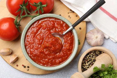 Photo of Homemade tomato sauce in bowl, spoon and fresh ingredients on light grey table, flat lay