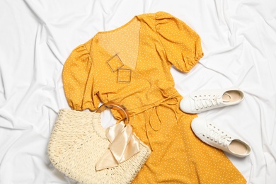 Flat lay composition with stylish yellow dress on white fabric