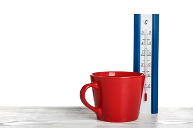 Photo of Thermometer and cup of hot tea on wooden table against white background. Space for text