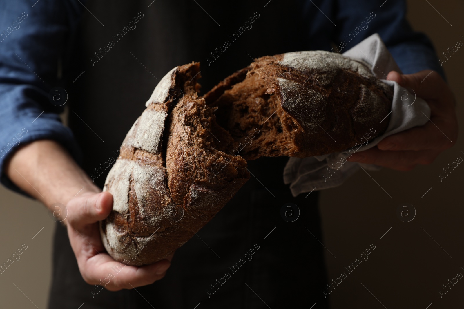 Photo of Man breaking loaf of fresh bread on dark background, closeup