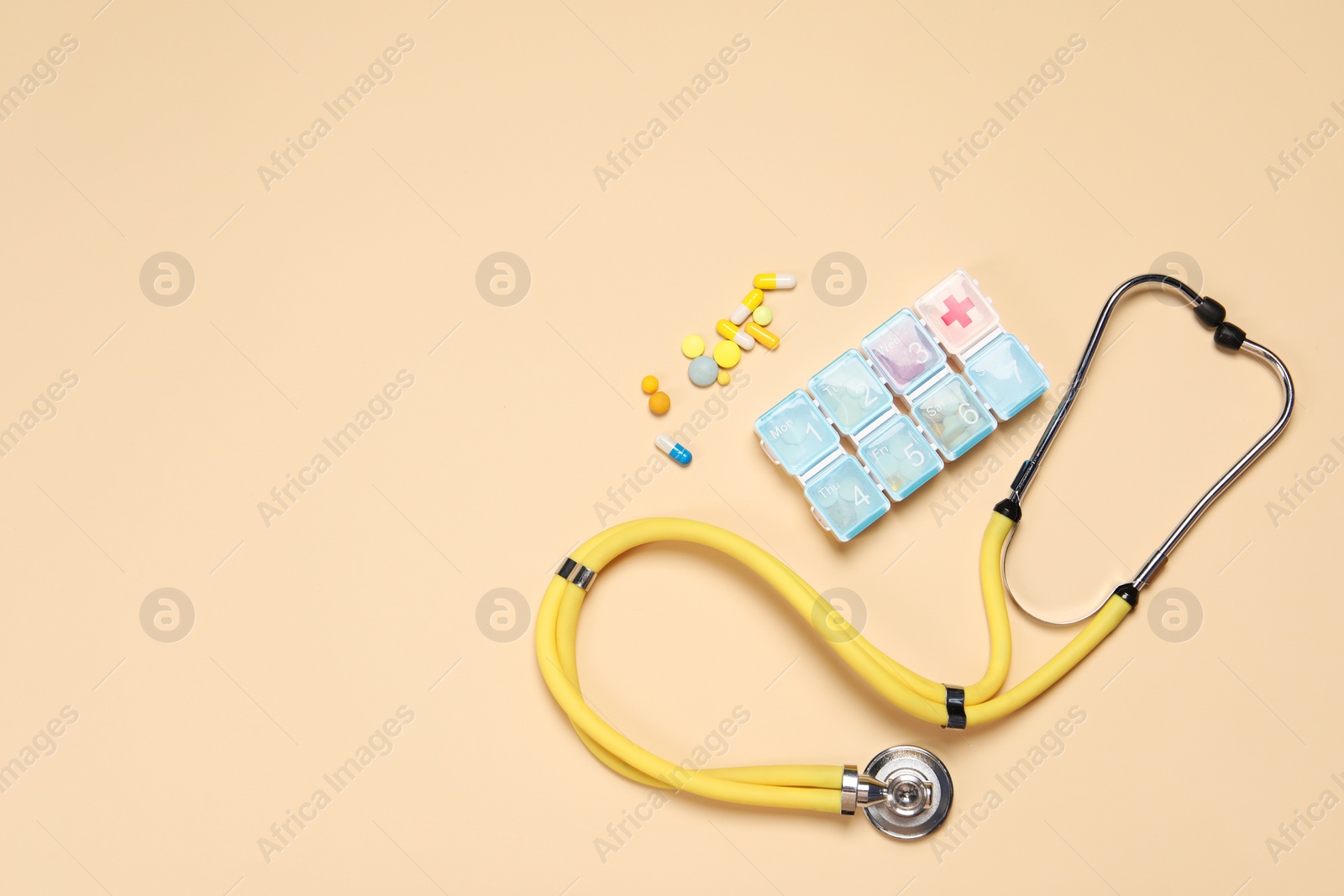 Photo of Stethoscope and pills on beige background, flat lay. Space for text