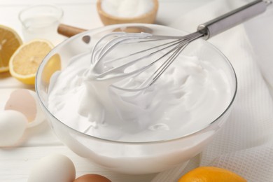 Bowl with whipped cream, whisk and ingredients on white wooden table, closeup