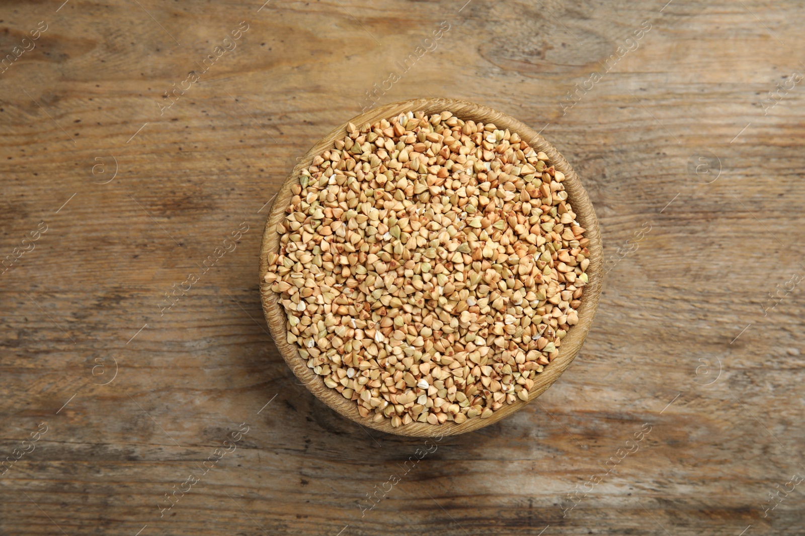 Photo of Uncooked green buckwheat grains in bowl on wooden table, top view