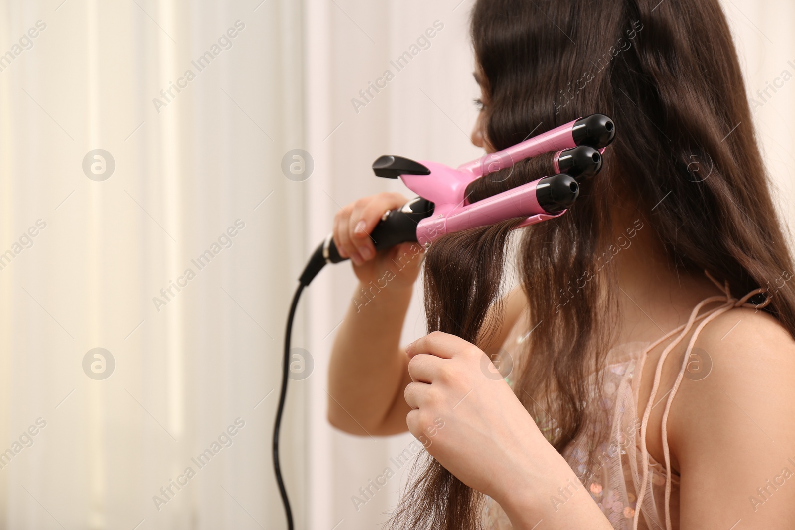 Photo of Young woman using modern curling iron on light background