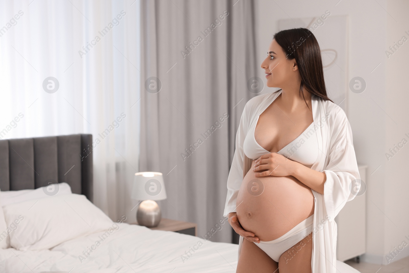 Photo of Beautiful pregnant woman wearing stylish comfortable underwear and robe in bedroom, space for text