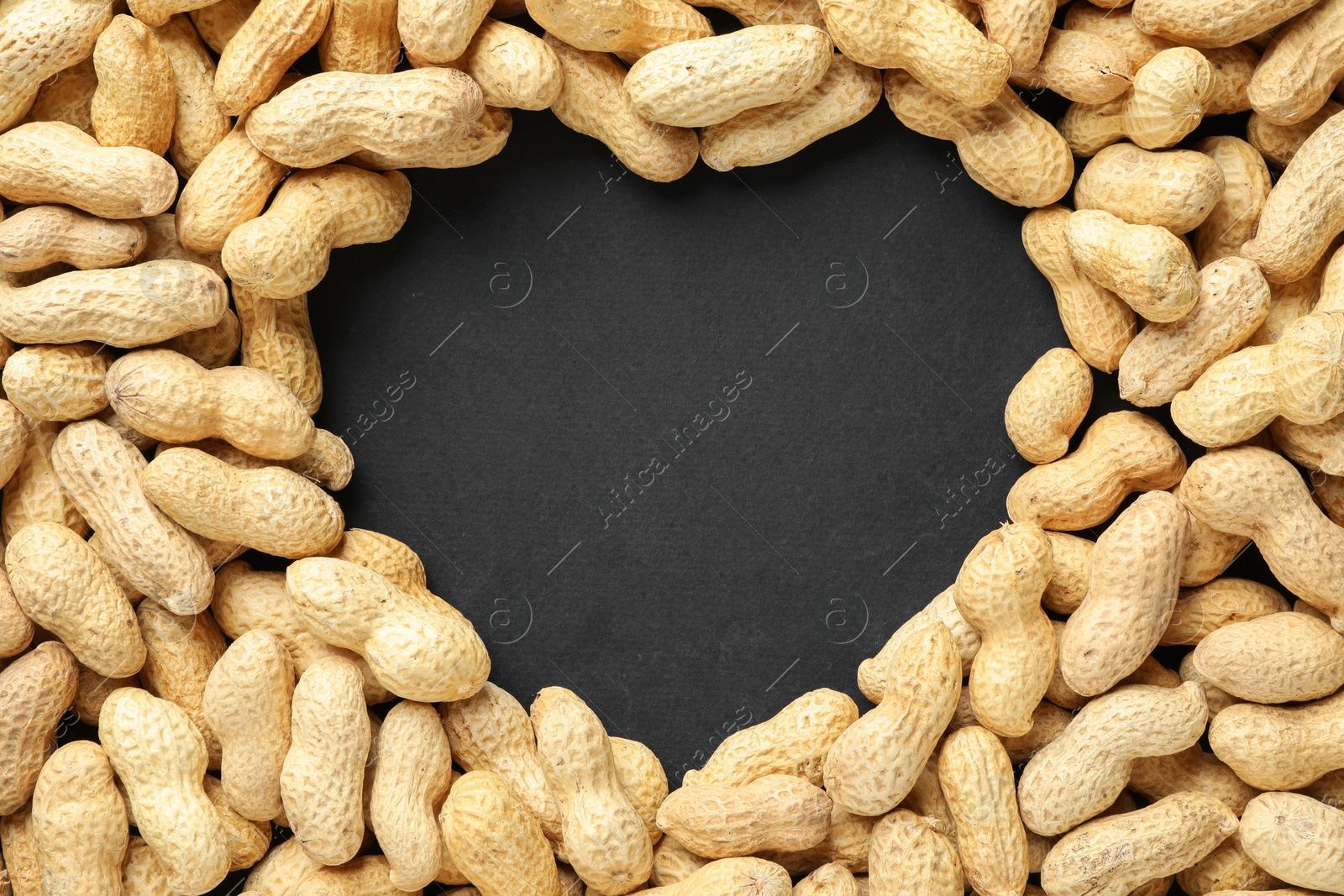 Photo of Heart made of unpeeled peanuts on black background, top view. Space for text