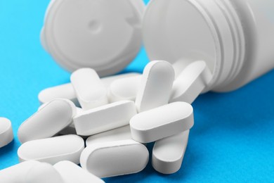 Photo of Vitamin pills and bottle on light blue background, closeup