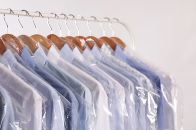 Photo of Hangers with shirts in dry cleaning plastic bags on rack against light background