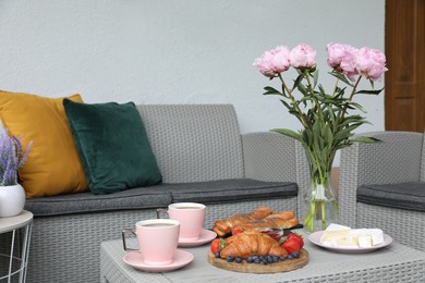 Photo of Morning drink, pastry, berries, cheese and vase with flowers on rattan table. Summer breakfast on terrace