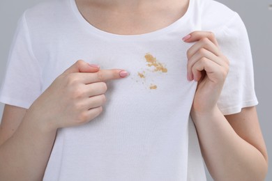 Woman showing stain on her t-shirt against light grey background, closeup