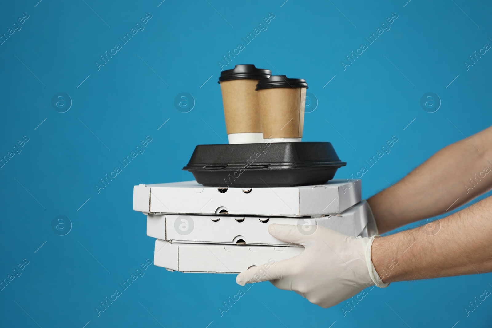 Photo of Courier in protective gloves holding order on blue background, closeup. Food delivery service during coronavirus quarantine