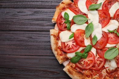 Photo of Delicious Caprese pizza with tomatoes, mozzarella and basil on dark wooden table, top view. Space for text