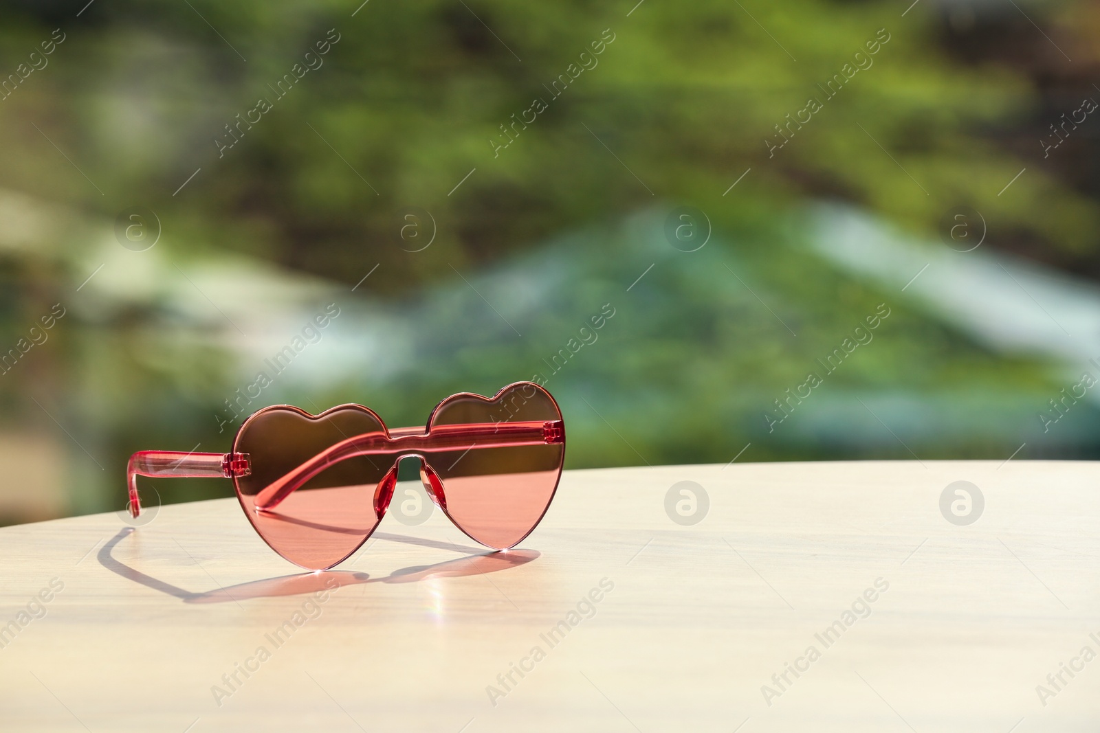Photo of Stylish heart shaped sunglasses on table against blurred background. Space for text