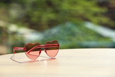 Stylish heart shaped sunglasses on table against blurred background. Space for text