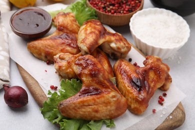 Photo of Fresh marinated chicken wings, spices and lettuce on light table, closeup