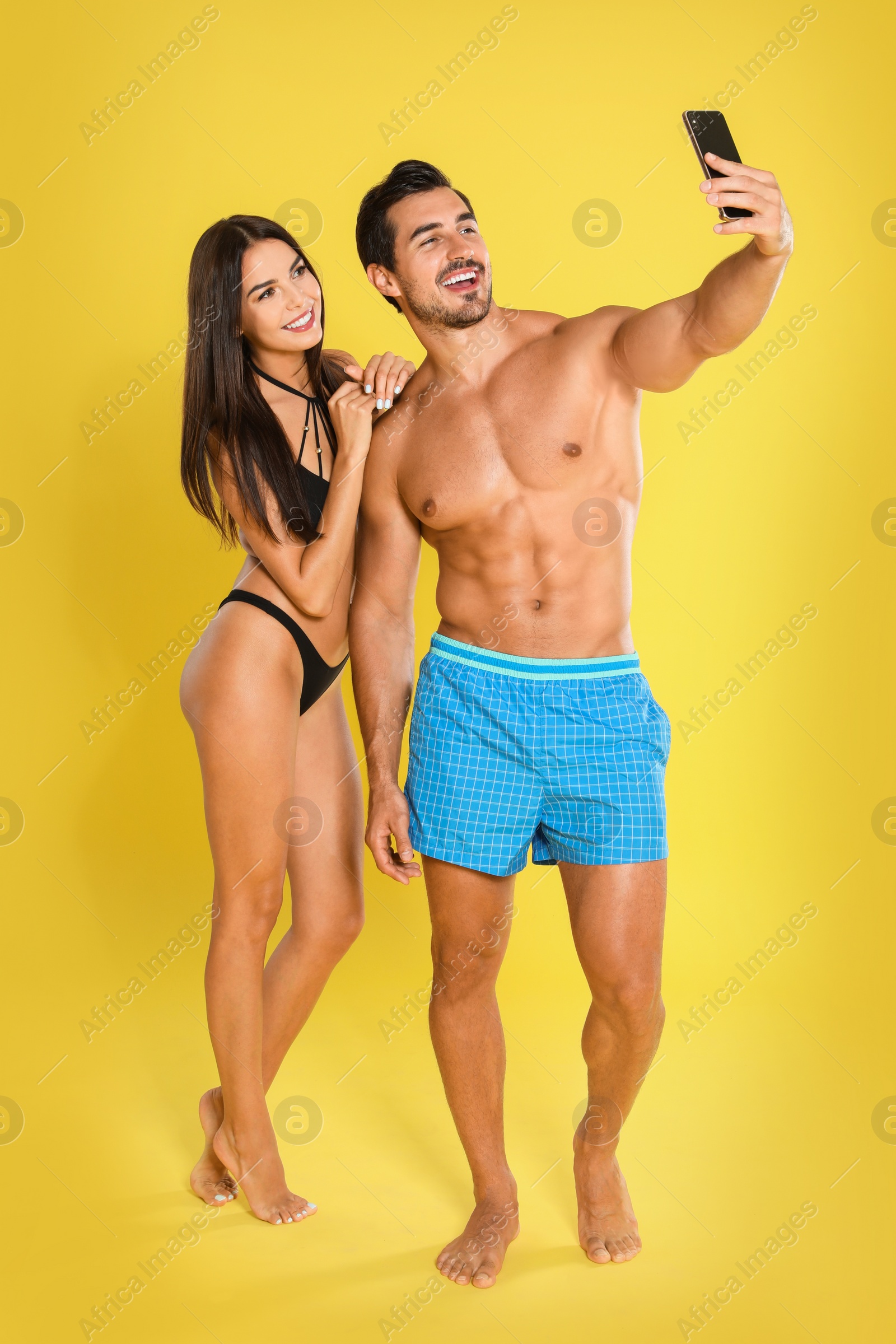 Photo of Young attractive couple in beachwear taking selfie on yellow background