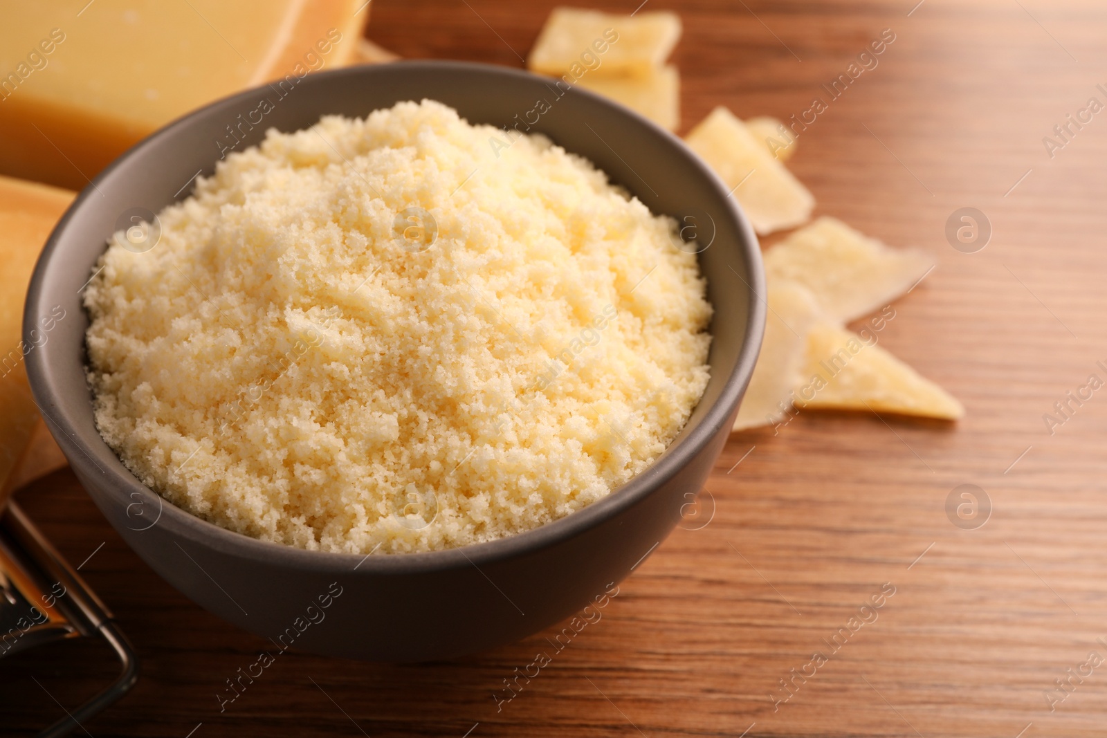 Photo of Delicious grated parmesan cheese in bowl on wooden table, closeup