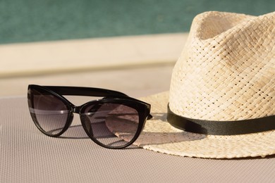 Photo of Stylish hat and sunglasses near outdoor swimming pool on sunny day