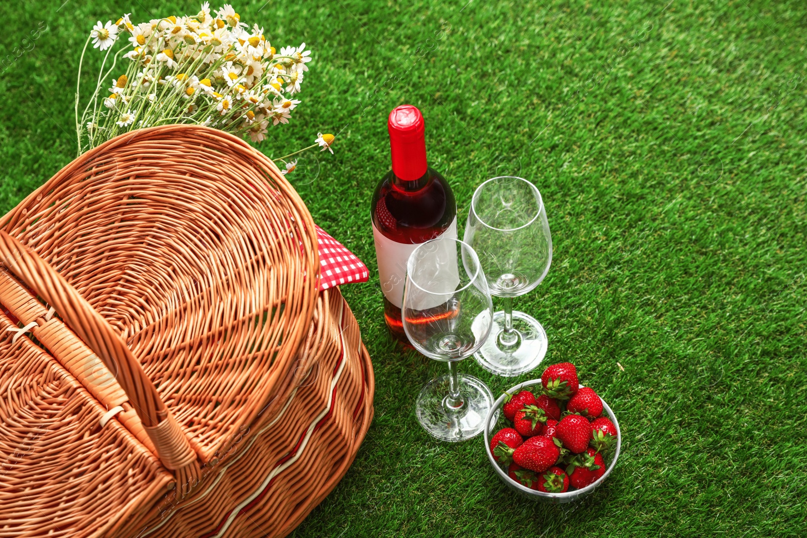 Photo of Picnic basket with wine and bowl of strawberries on grass
