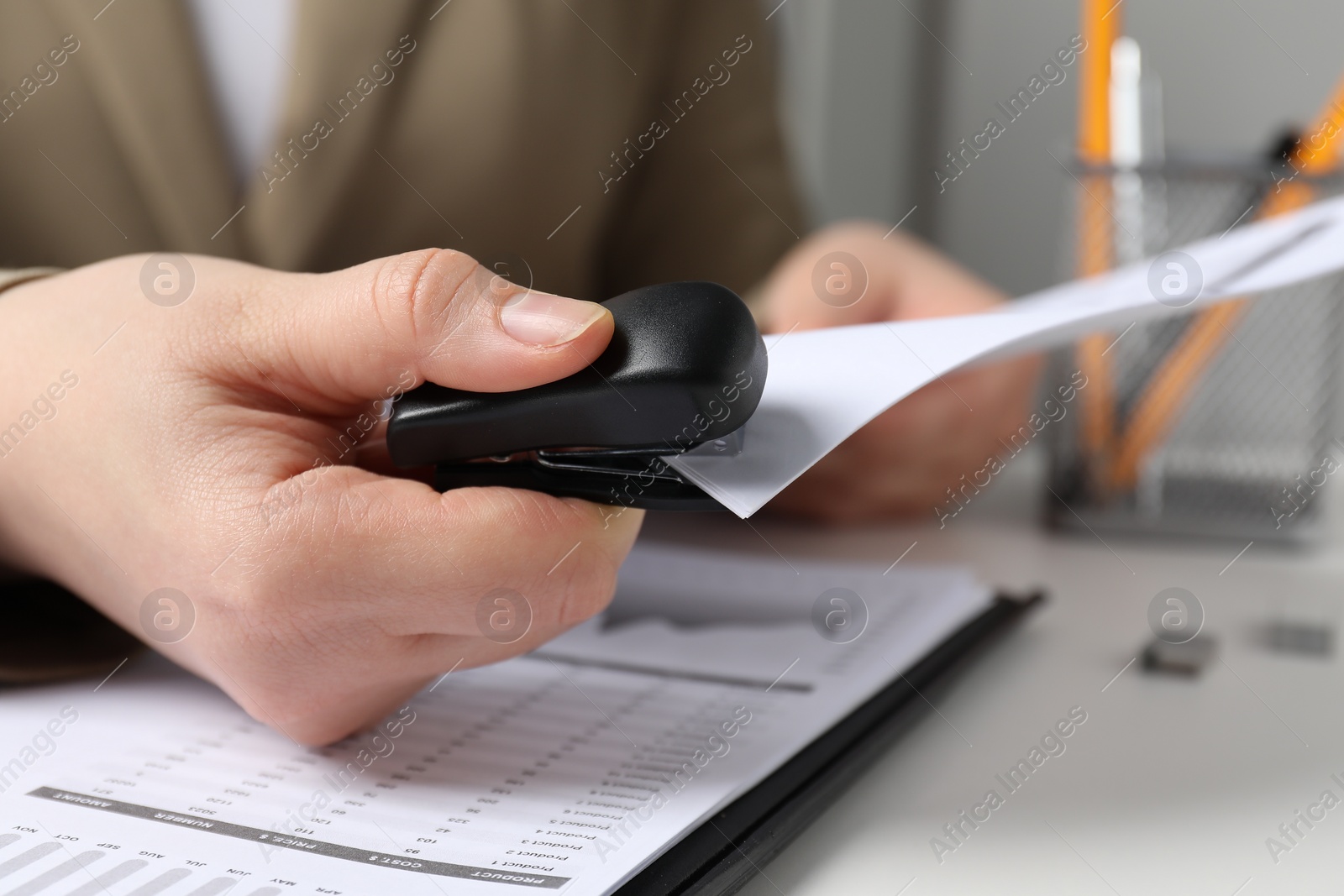 Photo of Woman with papers using stapler at white table indoors, closeup