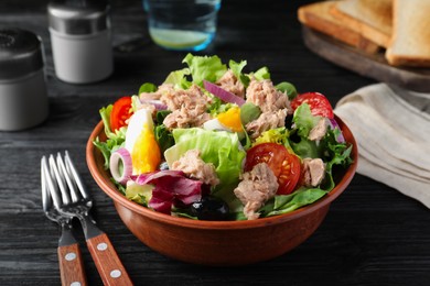 Photo of Bowl of delicious salad with canned tuna and vegetables served on black wooden table