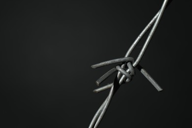 Metal barbed wire on dark grey background, closeup. Space for text