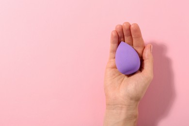 Photo of Woman with violet makeup sponge on pink background, top view. Space for text