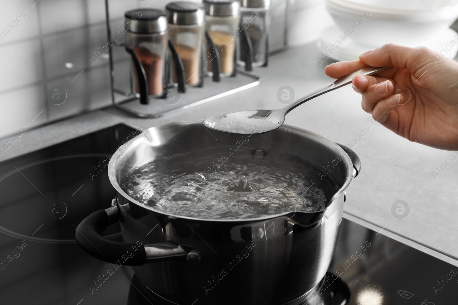 Photo of Woman salting boiling water in pot on stove, closeup