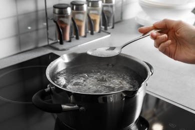 Woman salting boiling water in pot on stove, closeup