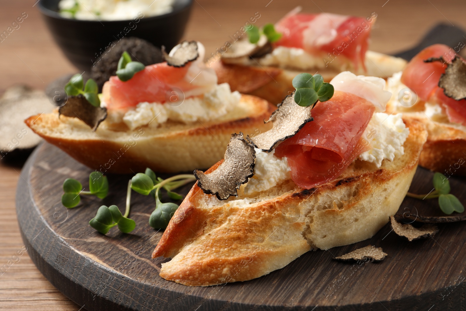Photo of Delicious bruschettas with cheese, prosciutto and slices of black truffle on wooden table, closeup