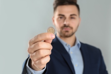 Young man holding coin against grey background, focus oh hand