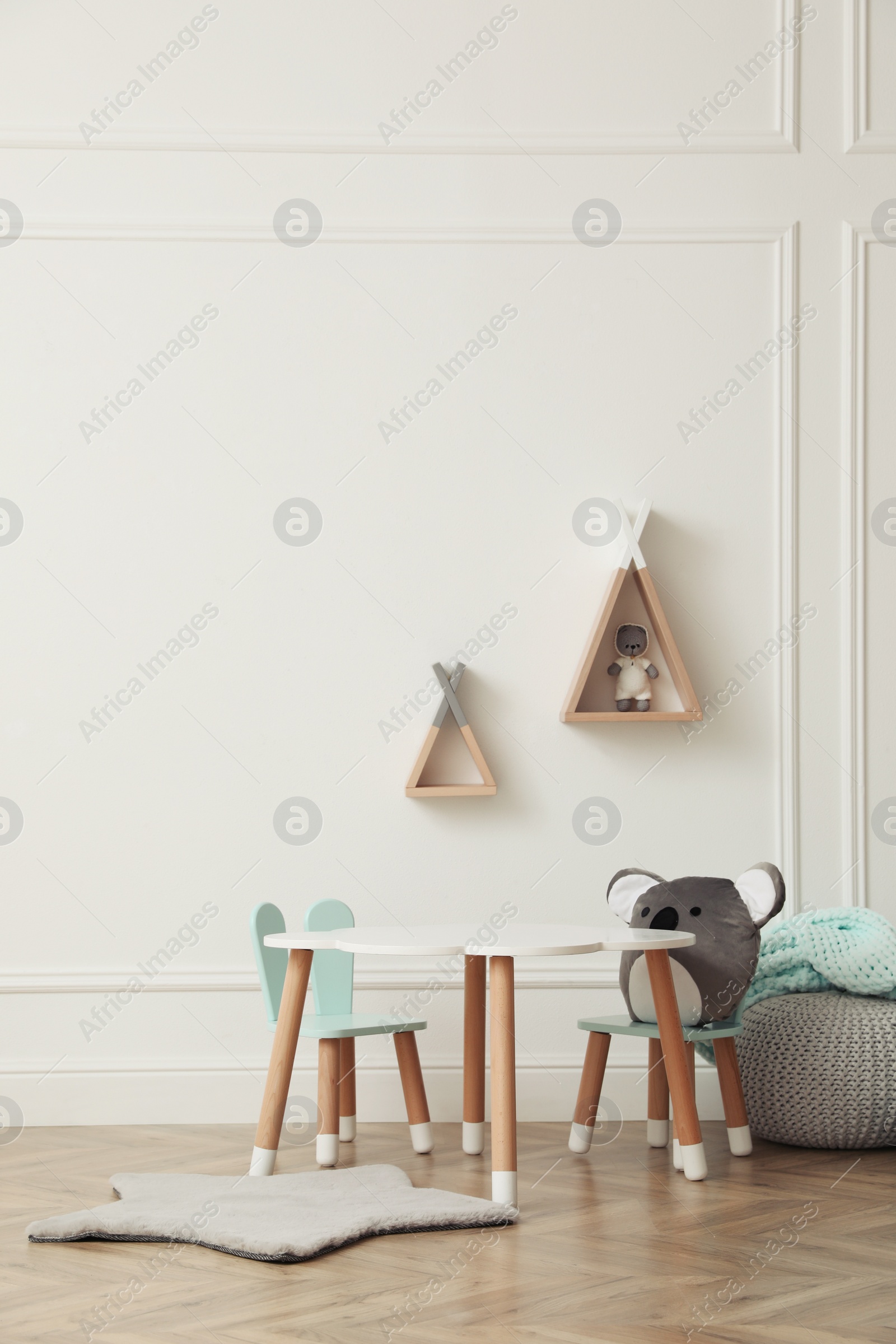 Photo of Cute child room interior with furniture, toys and wigwam shaped shelves on white wall