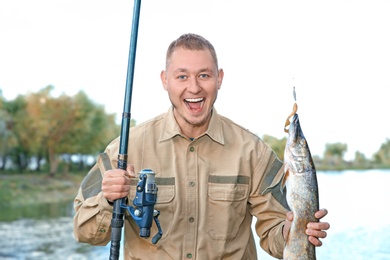 Photo of Man with rod and catch fishing at riverside. Recreational activity