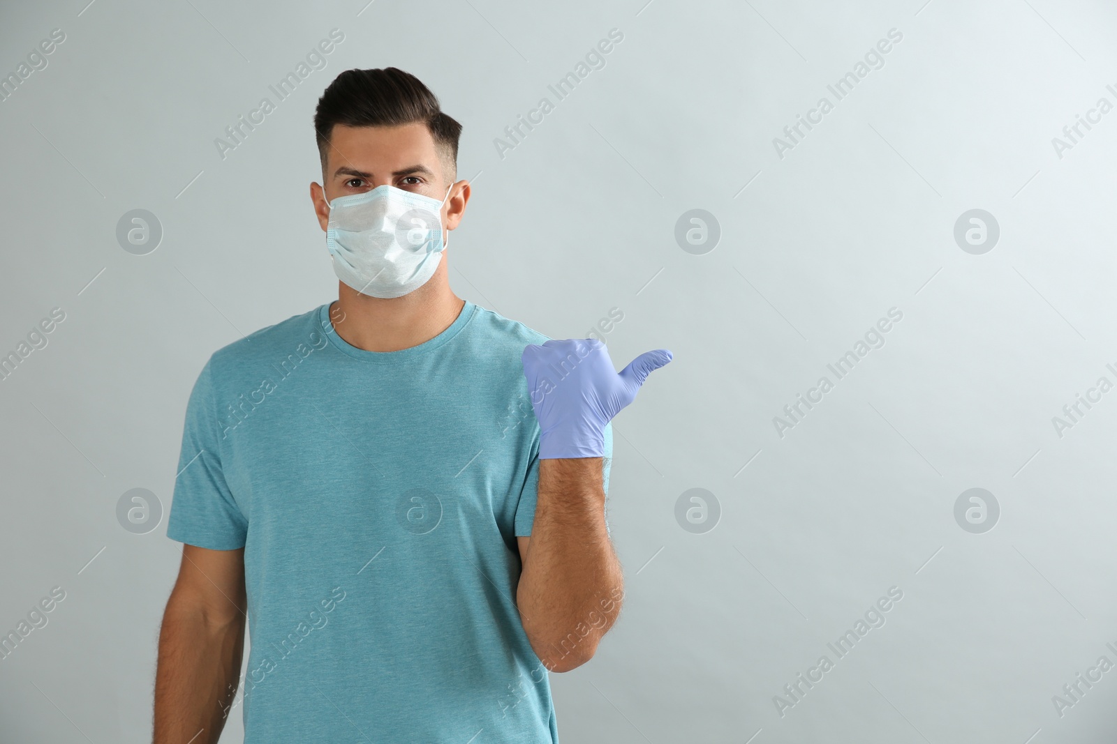 Photo of Man in protective face mask and medical gloves pointing at something on grey background. Space for text