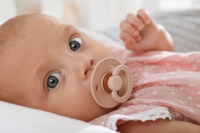 Photo of Cute little baby with pacifier lying in crib, closeup