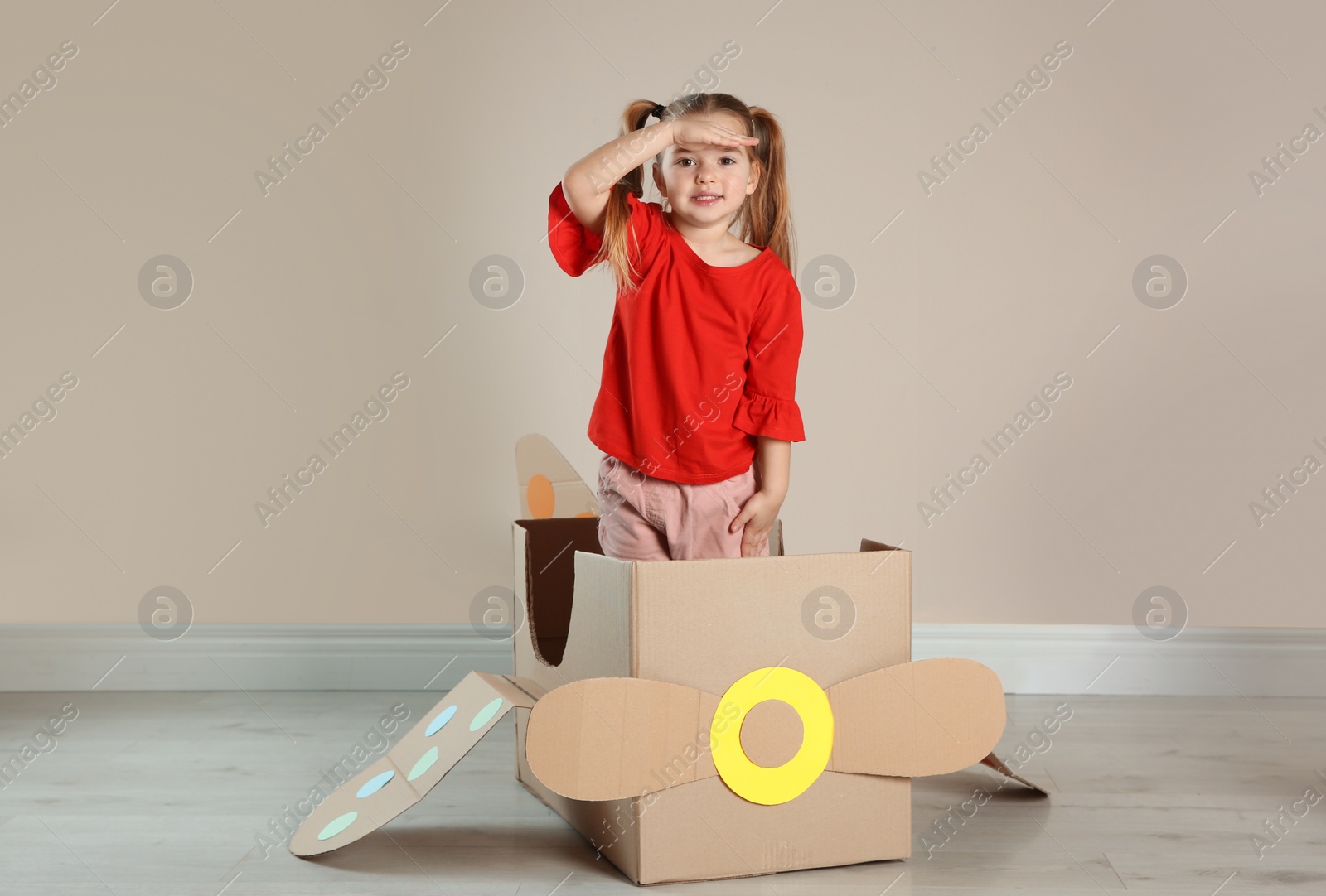 Photo of Cute little child playing with cardboard plane near beige wall