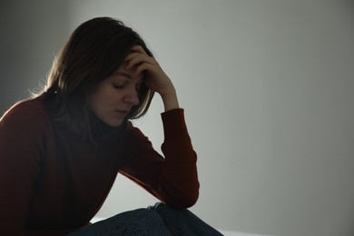 Photo of Sad young woman near grey wall indoors, space for text