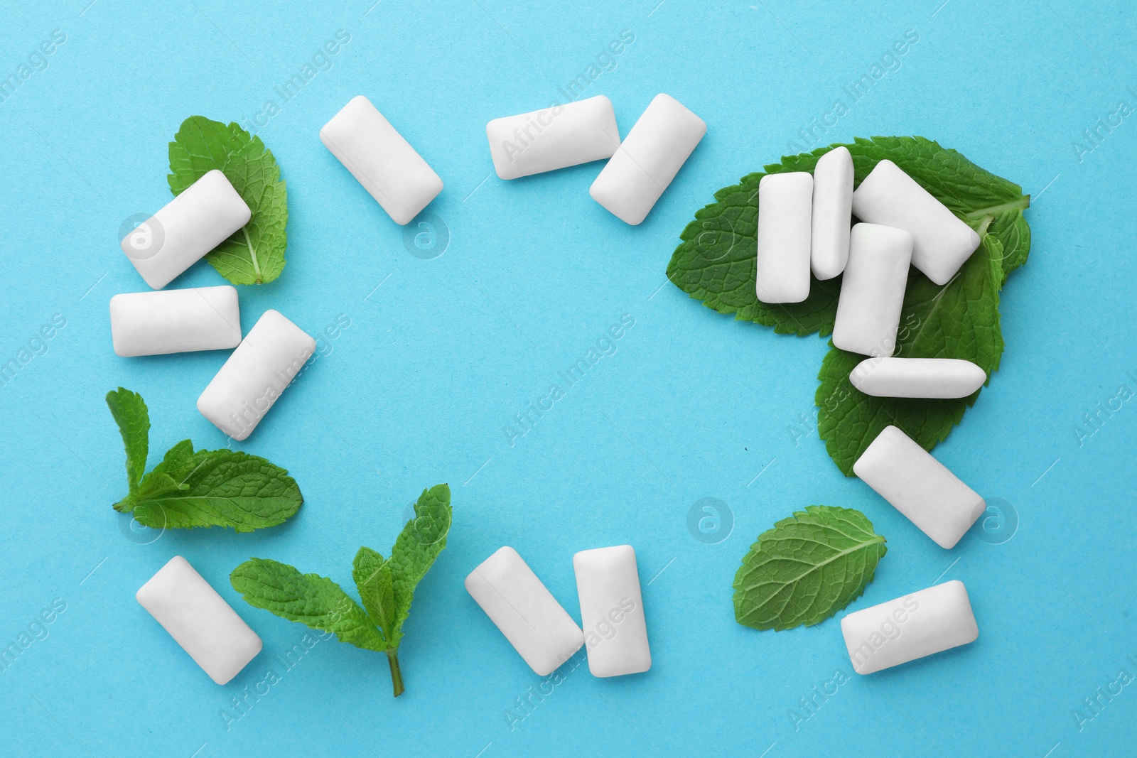 Photo of Frame made of tasty white chewing gums and mint leaves on light green background, flat lay. Space for text