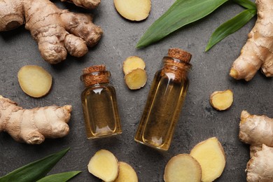Glass bottles of essential oil and ginger root on grey table, flat lay