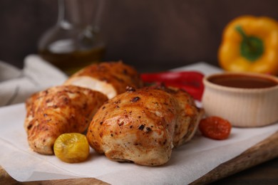 Photo of Baked chicken fillets and marinade on wooden table, closeup