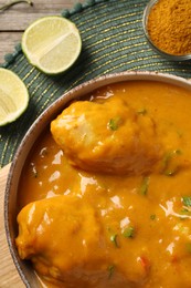 Photo of Tasty chicken curry, lime and spice on wooden table, top view