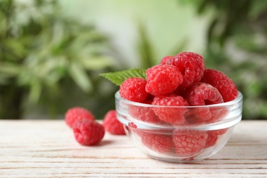 Photo of Delicious fresh ripe raspberries in bowl on white wooden table