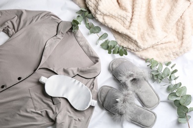 Photo of Flat lay composition with fluffy slippers and pajamas on white bedsheet. Comfortable home outfit