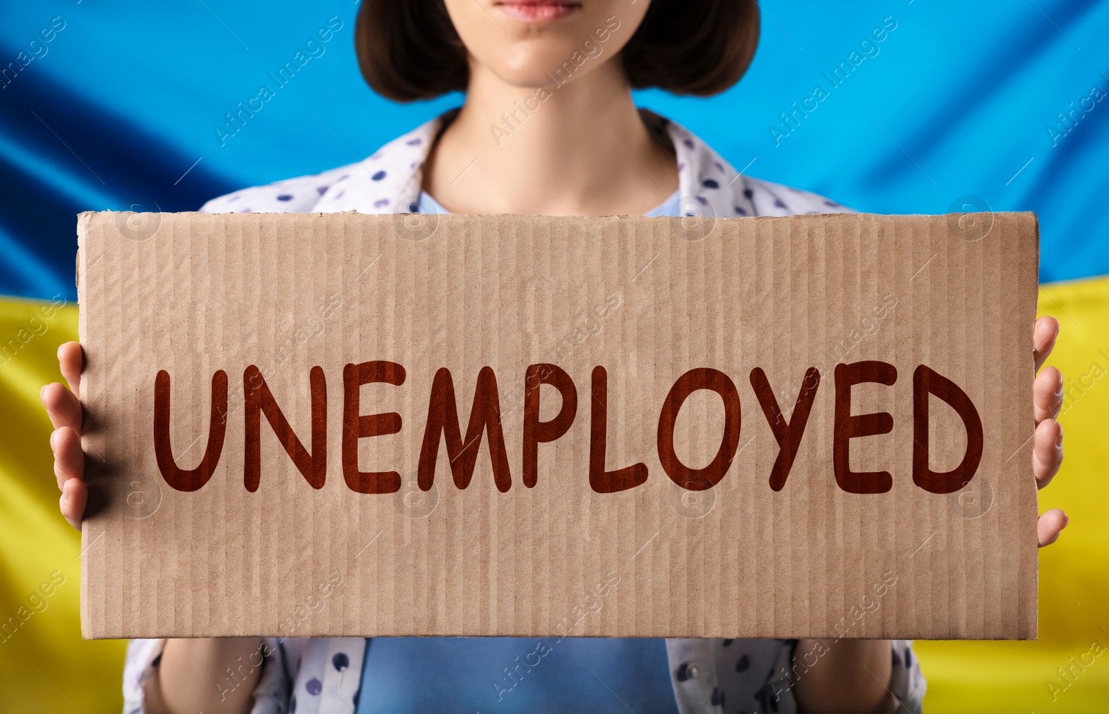 Image of Jobless due to war. Woman holding cardboard sheet with word Unemployed against Ukrainian flag, closeup