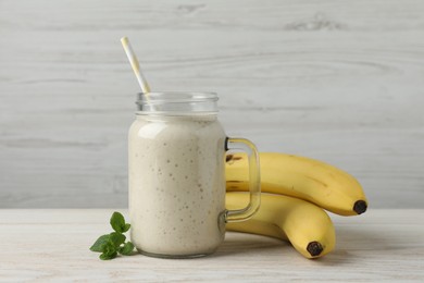 Photo of Mason jar with delicious fruit smoothie and fresh bananas on white wooden table