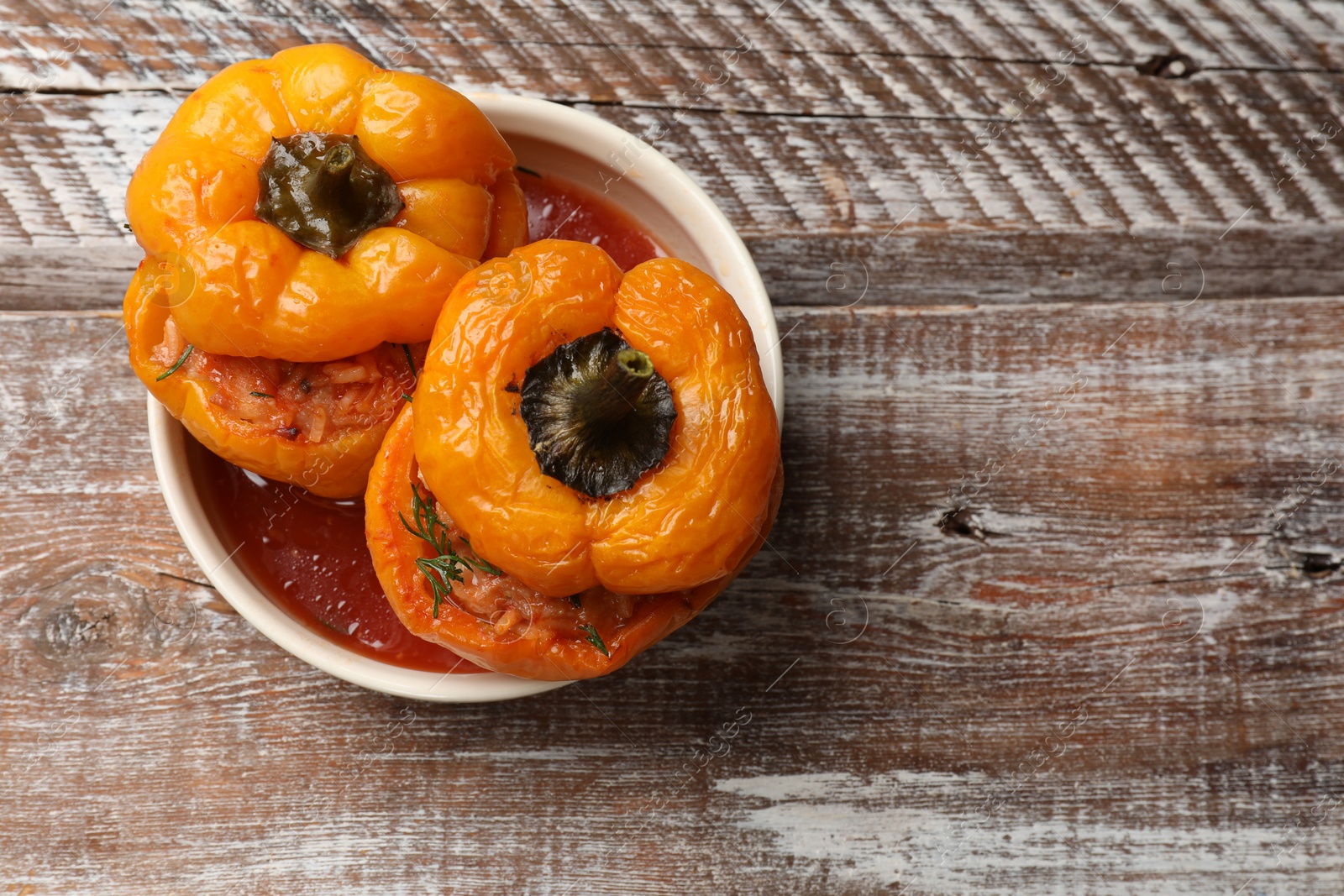 Photo of Tasty stuffed peppers in bowl on wooden rustic table, top view. Space for text