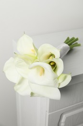 Photo of Beautiful calla lily flowers tied with ribbon on white chest of drawers indoors