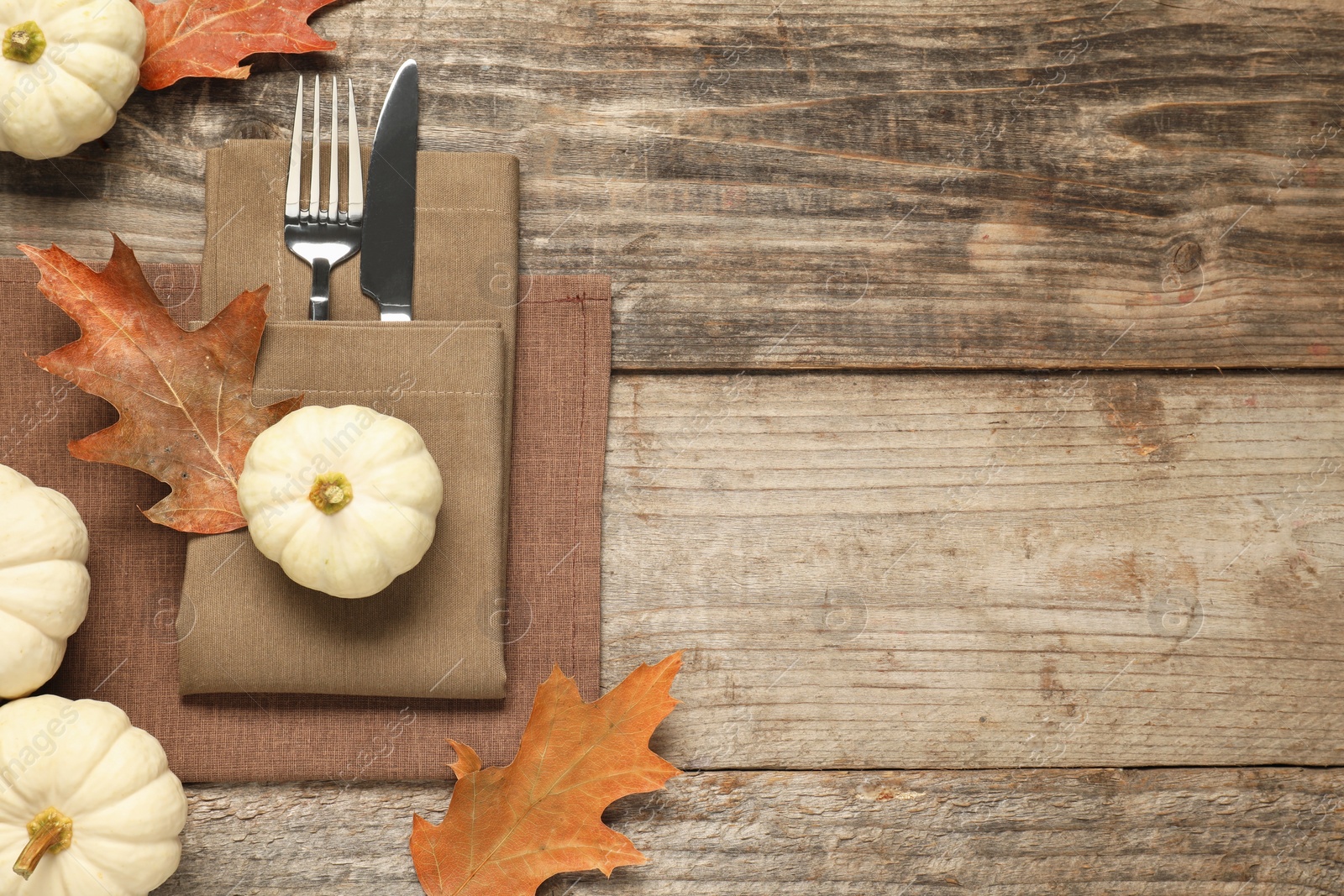 Photo of Cutlery, napkins and autumn decoration on wooden background, flat lay with space for text. Table setting