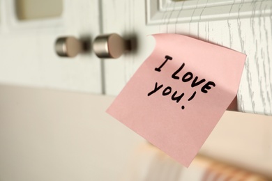 Photo of Sticky paper with words I Love You on door of kitchen cabinet indoors, closeup