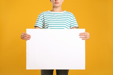 Woman holding white blank poster on yellow background, closeup. Mockup for design